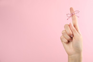 Woman showing index finger with tied bow as reminder on pink background, closeup. Space for text