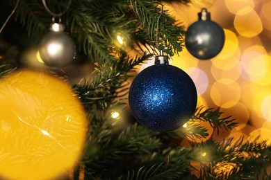 Beautiful shiny holiday baubles hanging on Christmas tree against blurred fairy lights, closeup