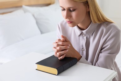 Religious young woman with Bible praying in bedroom