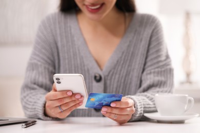 Woman with credit card using smartphone for online shopping at white table, closeup