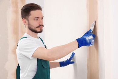 Worker in uniform plastering wall with putty knife indoors
