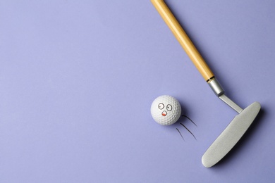 Golf ball with funny face flying away from club on lilac background - creative image. Top view