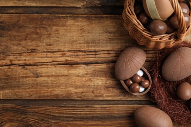 Flat lay composition with tasty chocolate eggs, wicker basket and decorative nest on wooden table. Space for text
