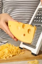 Woman grating fresh cheese at table, closeup