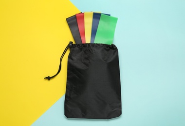 Bag with fitness elastic bands on color background, top view