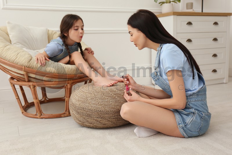 Young mother applying polish on daughter's nails at home