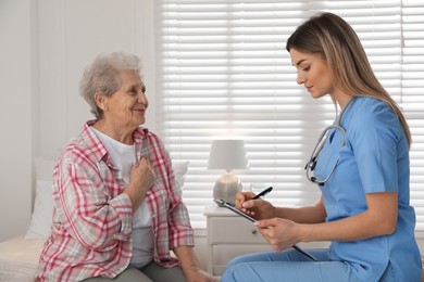 Young caregiver examining senior woman in room. Home health care service