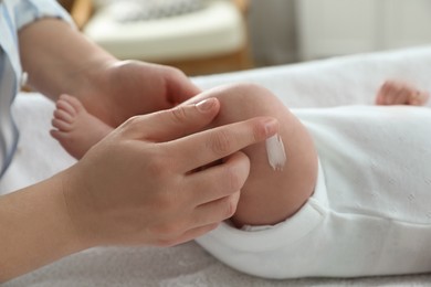 Mother applying body cream on her little baby indoors, closeup