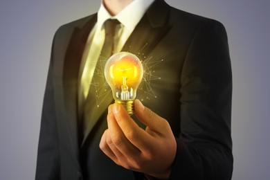 Glow up your ideas. Businessman holding light bulb on grey background, closeup