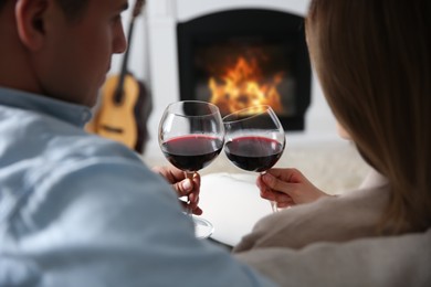 Couple toasting with glasses of wine near fireplace at home, back view