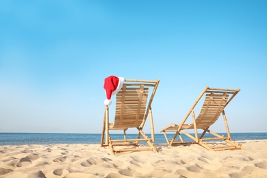 Photo of Sun loungers and Santa's hat on beach, space for text. Christmas vacation