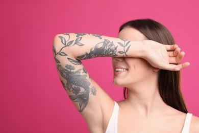 Beautiful woman with tattoos on arm against pink background