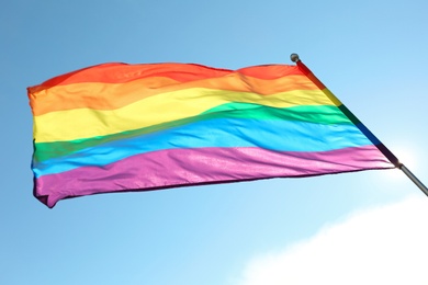 Bright rainbow gay flag fluttering against blue sky, bottom view. LGBT community