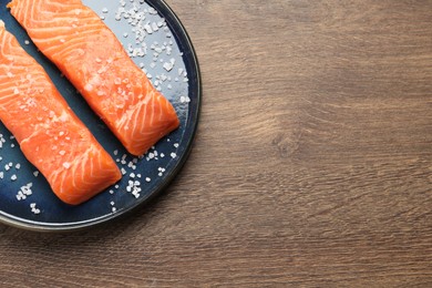 Photo of Fresh raw salmon with salt on wooden table, top view. Space for text