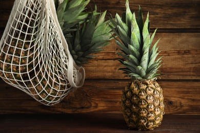 Photo of Bag and fresh juicy pineapples on wooden background