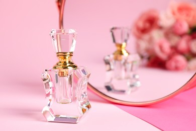 Bottle of perfume near mirror on pink background