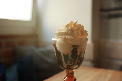 Photo of Delicious dessert with whipped cream in glass on table indoors, closeup