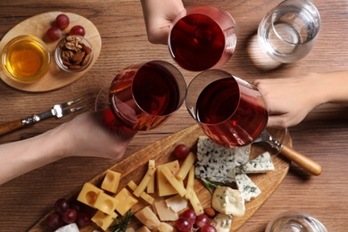 Women toasting with glasses of wine over cheese plate, top view
