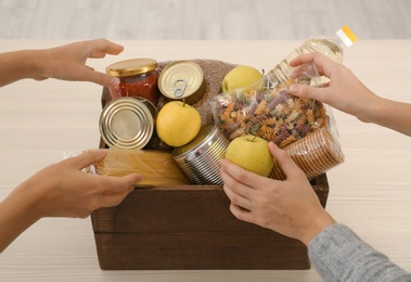 Women taking food out of donation box on wooden table, closeup