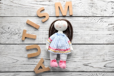 Word "Autism" and doll on wooden background, flat lay