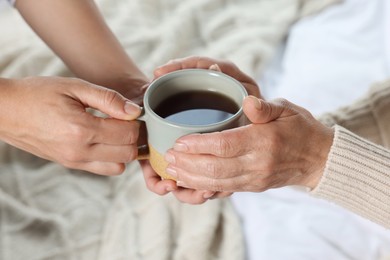 Caregiver giving drink to elderly woman at home, closeup