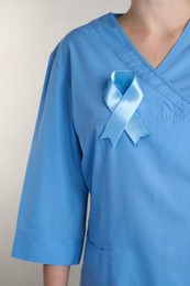 Photo of Doctor with light blue ribbon on grey background, closeup. World Diabetes Day