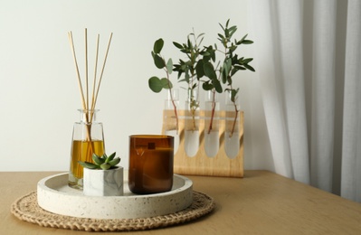 Photo of Beautiful plant, candle and aromatic reed air freshener on wooden table indoors, space for text. Interior elements