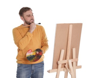 Man painting with brush on easel against white background. Young artist