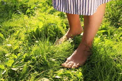 Photo of Woman walking barefoot on green grass, closeup. Space for text
