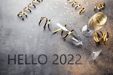 Text Hello 2022, glasses and serpentine streamers on grey table, above view