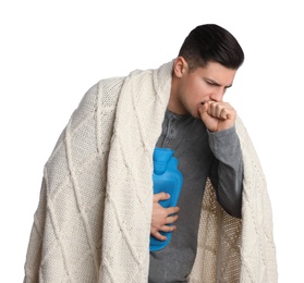 Ill man with hot water bottle and knitted blanket coughing on white background