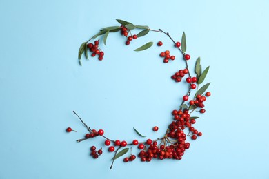 Photo of Red berries and leaves arranged in shape of wreath on light blue background, flat lay with space for text. Autumnal aesthetic
