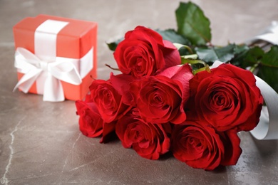 Beautiful red roses and gift box on grey table, closeup. Valentine's Day celebration