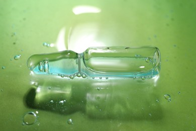 Pharmaceutical ampoule with medication in transparent gel on green background, closeup