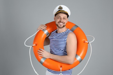 Happy sailor with orange ring buoy on grey background