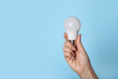 Woman holding LED light bulb on blue background, closeup. Space for text