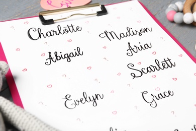 Clipboard with different baby names and toys on grey table, closeup
