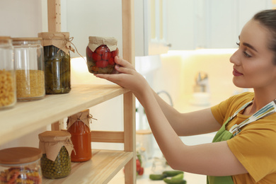 Woman putting jar of pickled vegetables on shelf indoors
