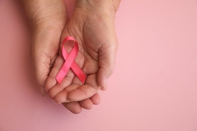 Senior woman holding pink ribbon on color background, top view with space for text. Breast cancer awareness
