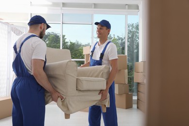 Moving service employees carrying armchair in room