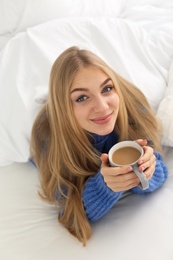 Beautiful young woman with cup lying in bed at home. Winter atmosphere