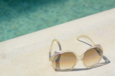 Stylish sunglasses near outdoor swimming pool on sunny day, space for text. Beach accessory