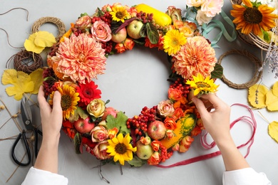 Florist making beautiful autumnal wreath with flowers and fruits at light grey table, top view
