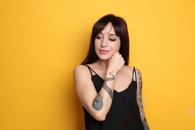 Beautiful woman with tattoos on arms against yellow background. Space for text