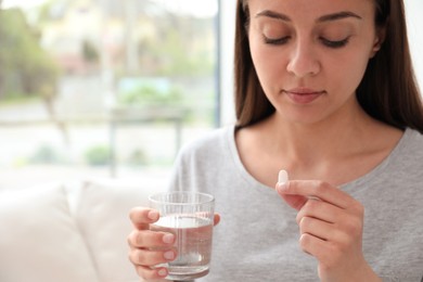 Young woman with glass of water taking pill at home, closeup