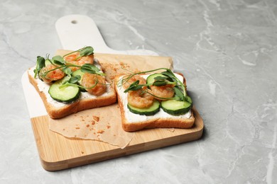 Tasty toasts with cream cheese, shrimps, cucumbers and microgreens served on grey marble table