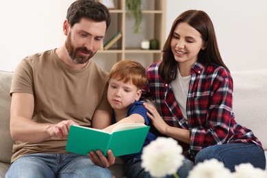 Happy parents with their child reading book on couch at home