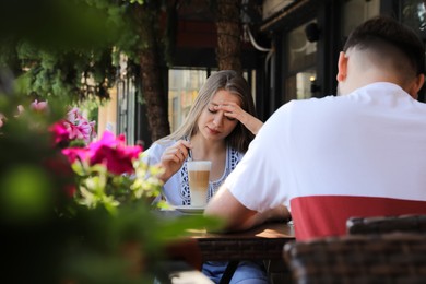 Photo of Young woman having boring date with guy in outdoor cafe
