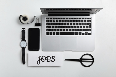 Photo of Flat lay composition with word JOBS, laptop, smartphone and stationery on white table. Career concept