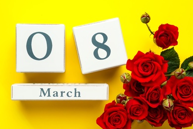 Wooden block calendar with date 8th of March and roses on yellow background, flat lay. International Women's Day